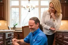 Appliance repair technician fixing a wall oven while the homeowner watches